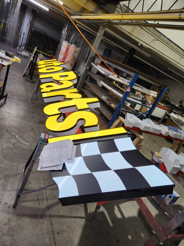 Yellow auto parts channel letters with a checkered flag on the shop floor